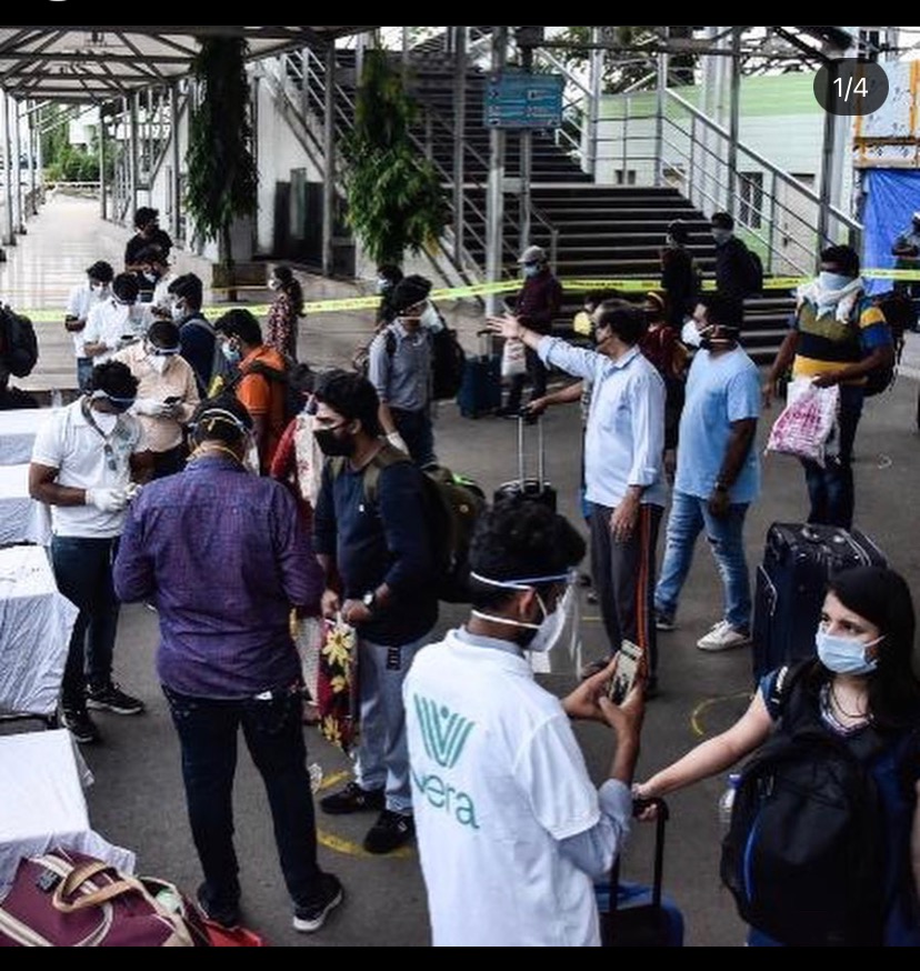 Returning passengers in masks queued at transit hub processing point · Vera intake