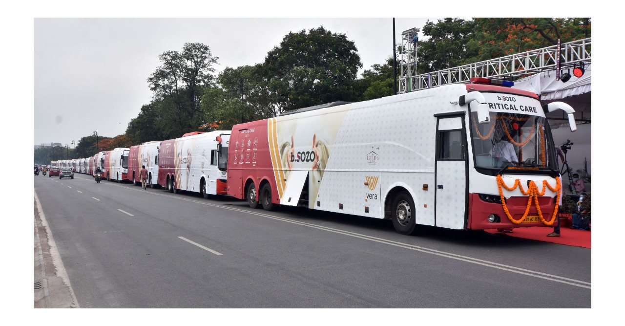 Fleet of b.SOZO Critical Care 24x7 buses lined up at the Hyderabad launch · marigold garlands · Vera logo on the side · multiple identical coaches converted to mobile ICUs
