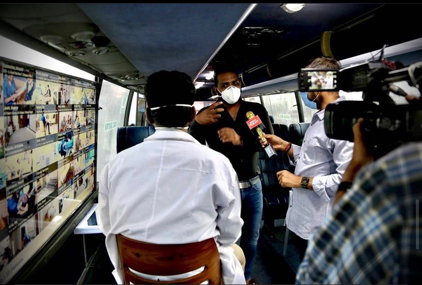 Dharma being interviewed by the India Today Group inside the iMASQ bus during operation · TV camera and reporter visible · service-icon screens on walls