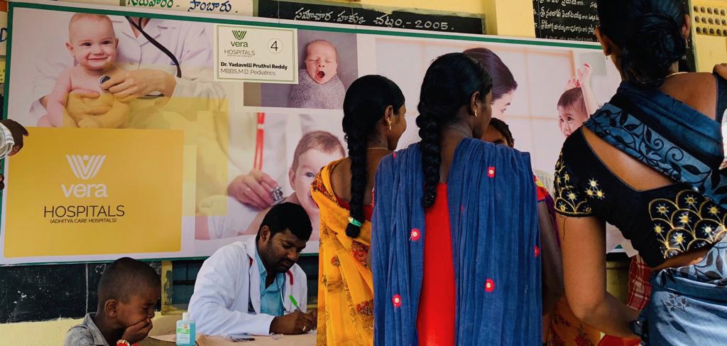 Vera Hospitals (Adhitya Care Hospitals) banner at the Nalgonda Smart Health Camp · Dr. Yadavelli Pruthvi Reddy consulting with mothers and children
