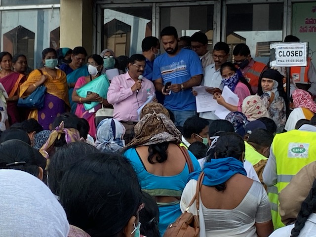 Large crowd of healthcare workers, GHMC staff and Vera personnel at a coordination briefing for COVID transit hub deployment · masked · holding intake forms