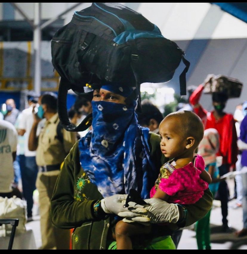 Migrant worker carrying luggage on head and a small child in arm at the Vera processing point · pandemic-era return migration